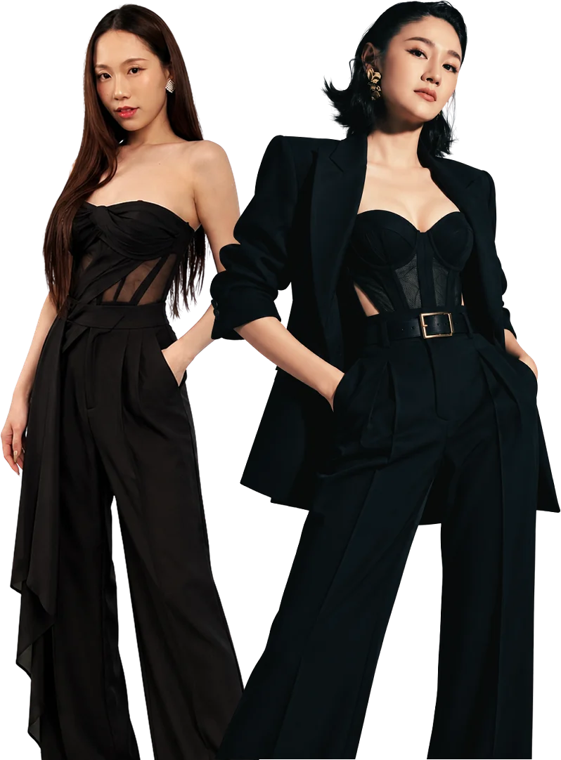 Goey and Nico in black: one in a strapless corset top and wide trousers, the other in a blazer over a corset and belted trousers
