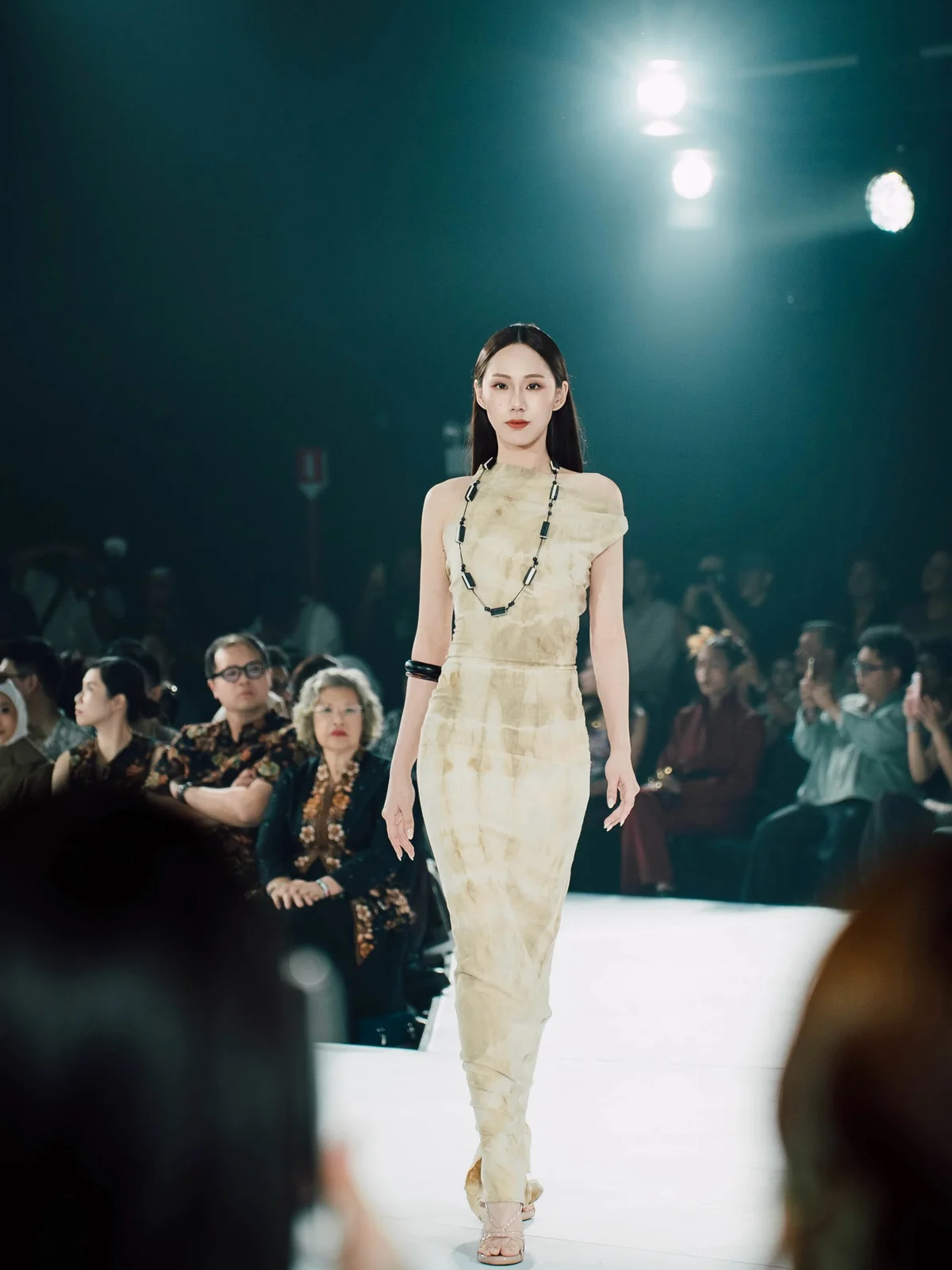 Nico walking the runway in a draped ivory dress, the audience seated on either side