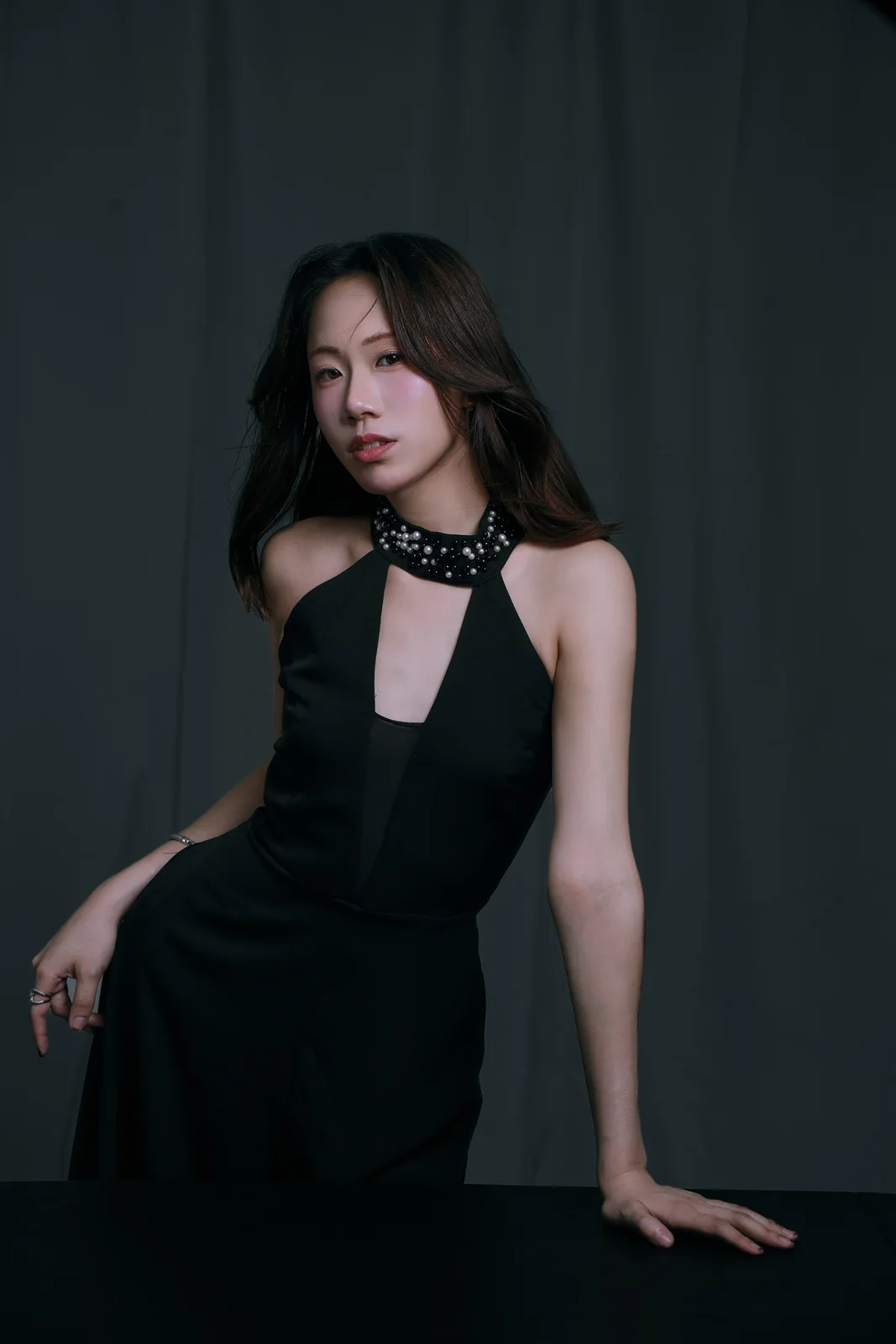 Nico in a black halter dress with a jewelled collar, leaning on a dark table with one arm outstretched