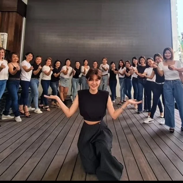 A group posing workshop: a teacher kneels and demonstrates a pose in front of a long line of students