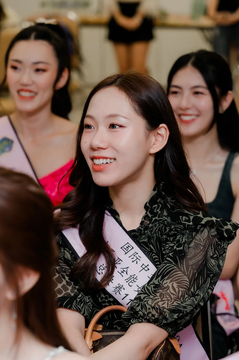 Smiling contestants wearing sashes, seated together during the pageant programme
