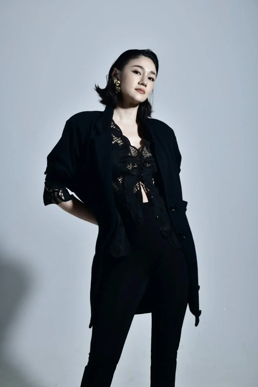 Studio portrait: a model in a black jacket over a lace top, one hand on her hip